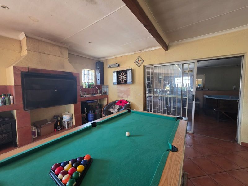 Entertainment room featuring a built-in braai, tiled flooring, and an exposed ceiling beam, with direct access to an adjacent living area via sliding doors.