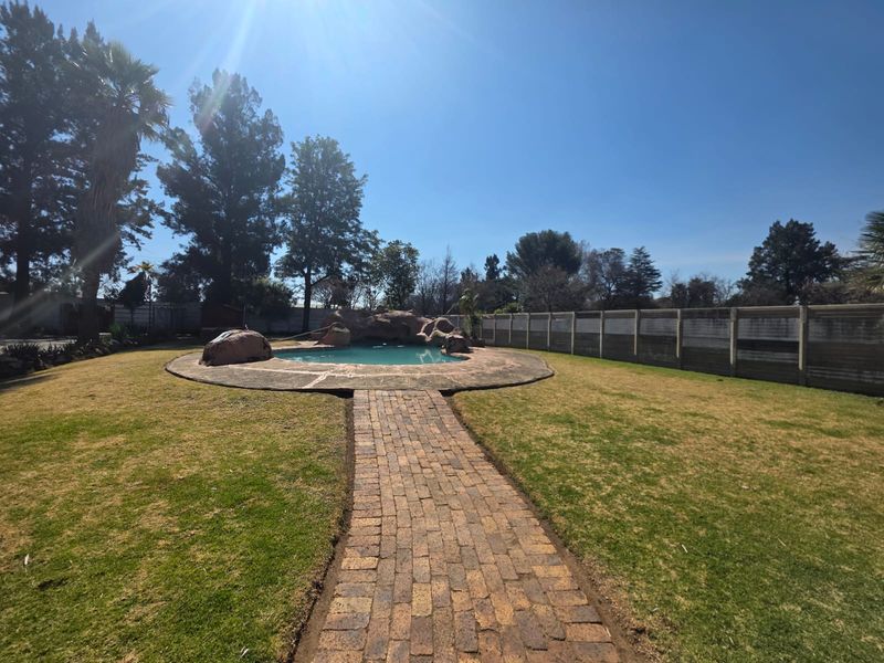 Spacious backyard featuring a swimming pool with a decorative rock feature, a brick paved walkway, and a secure precast concrete boundary wall.