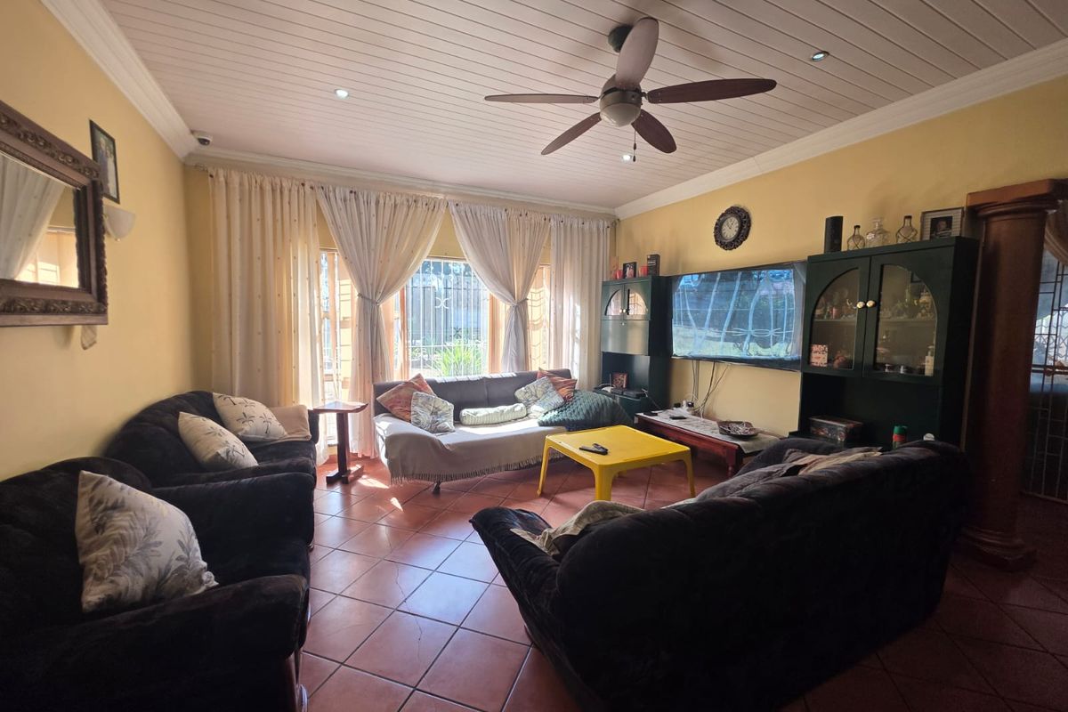 A living room featuring tiled flooring, a tongue and groove ceiling with a central fan, and large windows with curtains.