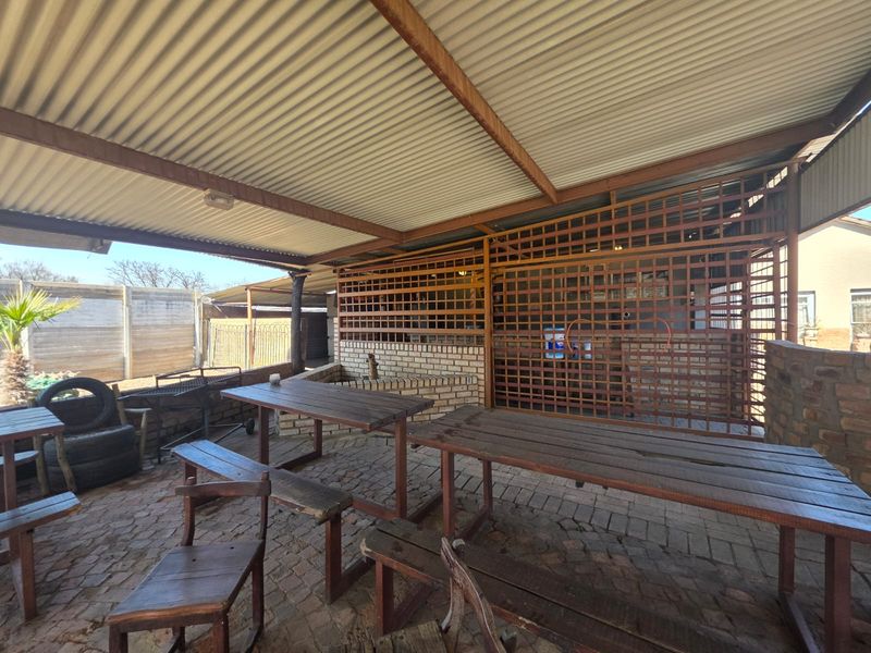 Covered outdoor patio area featuring a corrugated metal roof, brick paving, and a timber lattice screen, providing a rustic space for outdoor entertainment.