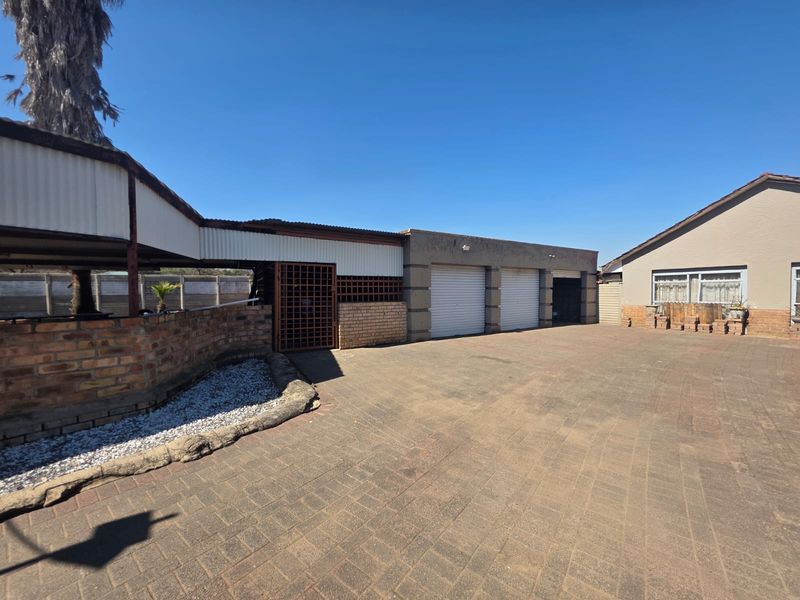 Spacious paved driveway leading to a triple garage with a covered outdoor area and brick boundary walling.
