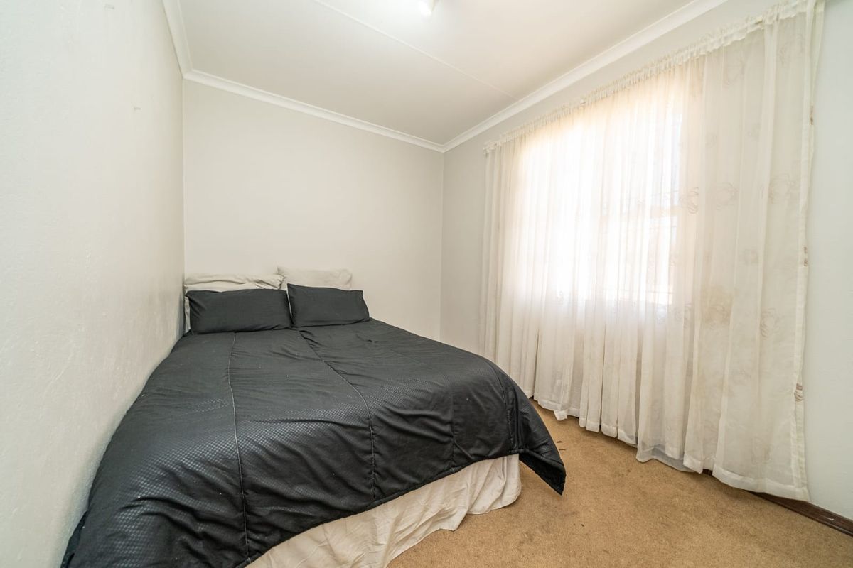 A compact bedroom featuring neutral wall finishes, carpeted flooring, and a large window with sheer curtains.
