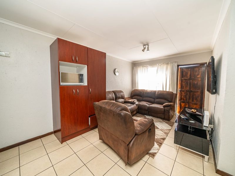 A living room featuring tiled flooring, built-in cabinetry, and a timber entrance door, offering a functional space with potential for cosmetic updates.