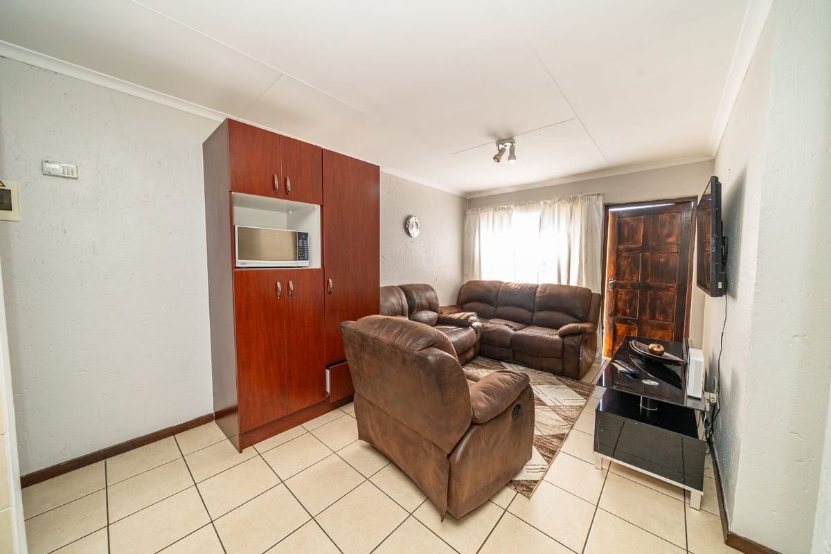 A living room featuring tiled flooring, built-in cabinetry, and a timber entrance door, offering a functional space with potential for cosmetic updates.