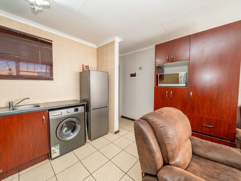 Functional laundry area featuring built-in cabinetry, tiled splashback, stainless steel sink, and tiled flooring with integrated appliance space.