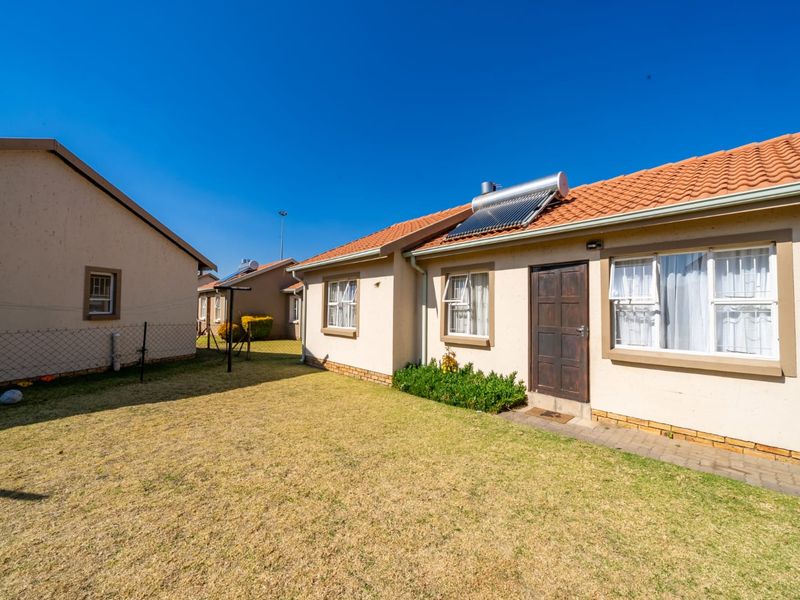 Rear view of the property featuring a lawn, paved walkway, and a solar water heating system installed on the tiled roof.