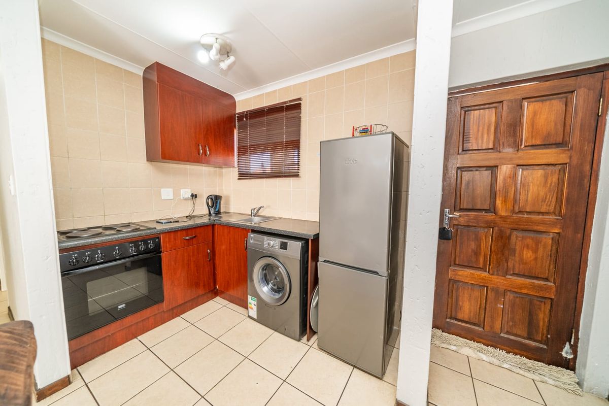 Compact kitchen featuring built-in wooden cabinetry, electric oven and hob, tiled splashback, and direct access via a solid timber door.