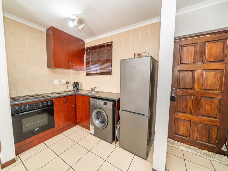 Compact kitchen featuring built-in wooden cabinetry, electric oven and hob, tiled splashback, and direct access via a solid timber door.