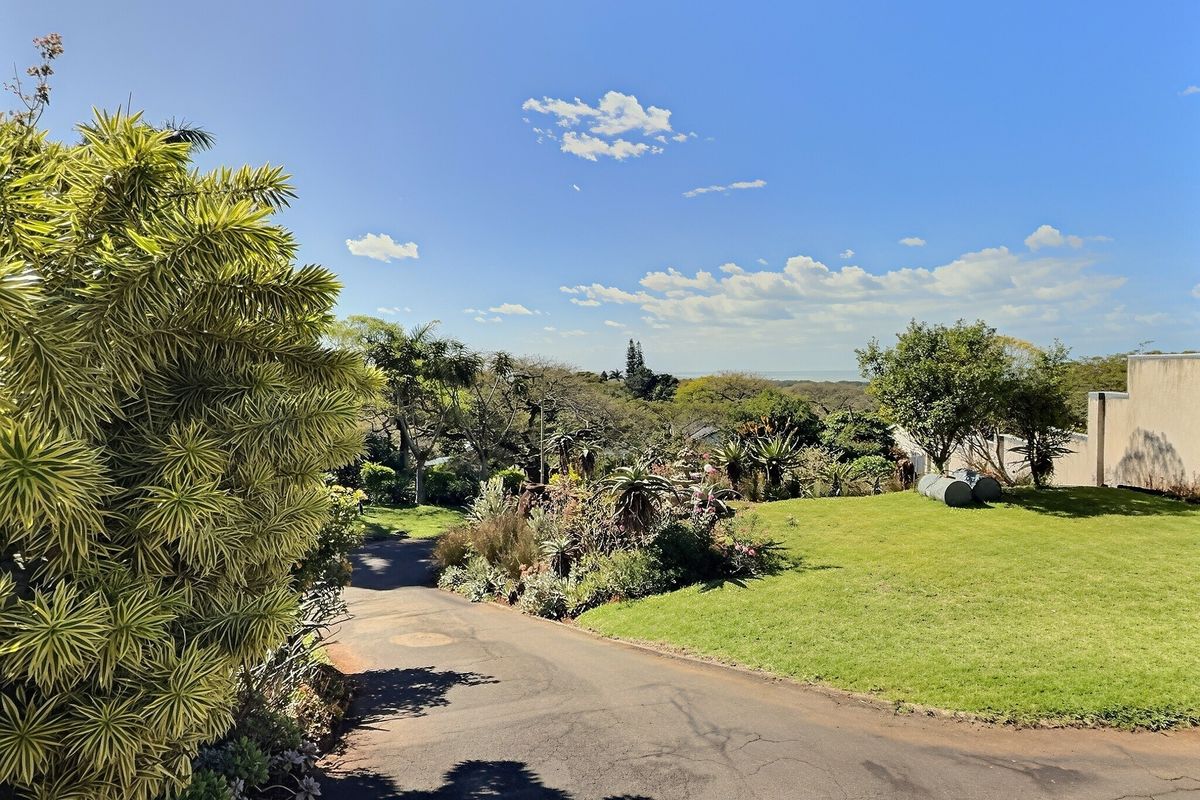 A well-maintained garden area featuring a paved driveway, lush lawn, and established landscaping with a view of the surrounding greenery.