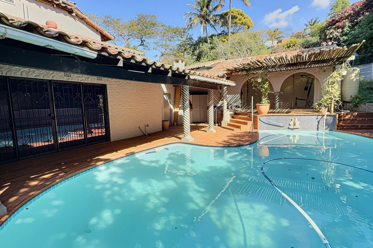 Outdoor pool area featuring wooden decking, a covered pergola, and decorative columns, providing a relaxed space for outdoor entertainment and leisure.