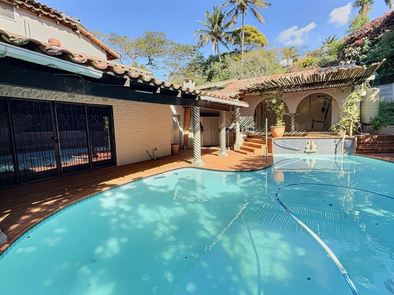 Outdoor pool area featuring wooden decking, a covered pergola, and decorative columns, providing a relaxed space for outdoor entertainment and leisure.