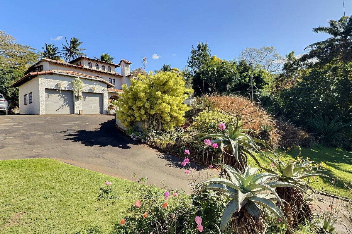 Front view of a Mediterranean-style house featuring a double garage, paved driveway, and established landscaped garden.