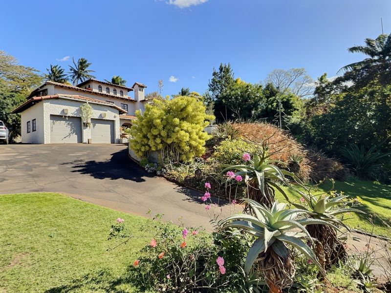 Front view of a Mediterranean-style house featuring a double garage, paved driveway, and established landscaped garden.