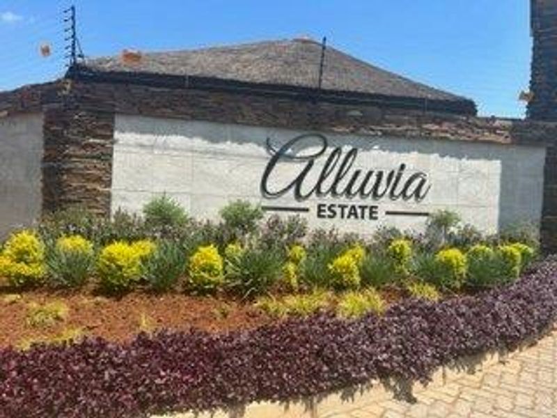 The entrance signage and landscaped garden area of Alluvia Estate, featuring stone cladding and secure electric fencing.