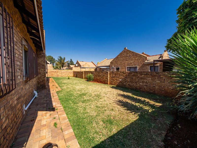 A private rear garden featuring a brick-paved walkway, established lawn, and high perimeter brick boundary walls for added privacy.