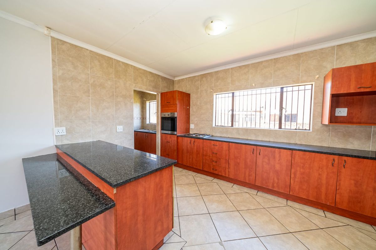 A functional kitchen featuring wooden cabinetry, granite countertops, built-in oven, hob, and tiled finishes, with an adjacent scullery area.