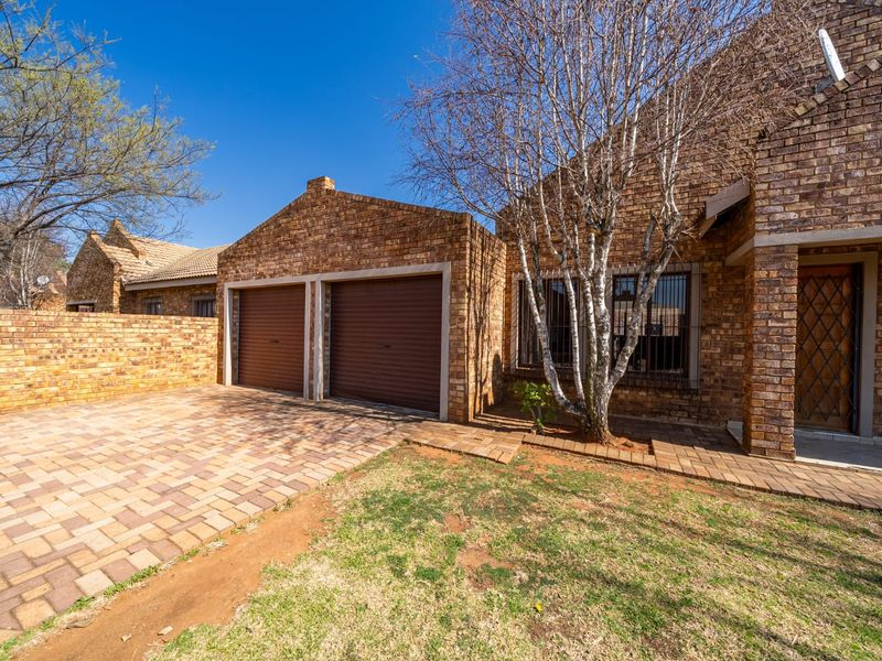 Front exterior view of a townhouse featuring a double garage, brick facade, paved driveway, and security features.