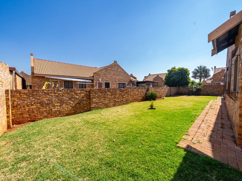 A private rear garden featuring a well-maintained lawn, brick boundary walls, and a paved walkway alongside the townhouse structure.