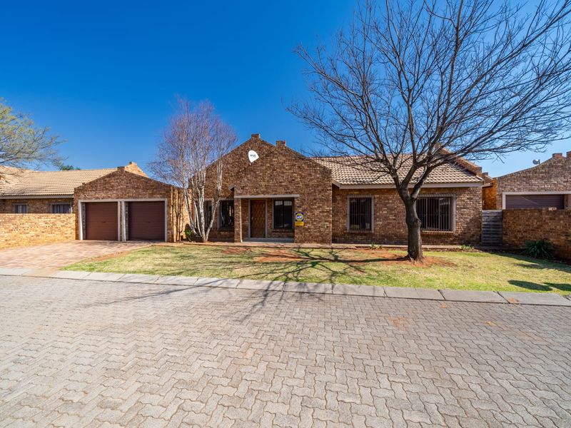 A well-maintained face-brick townhouse featuring a double garage, paved driveway, and secure window bars, set within a neat residential complex.