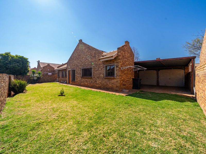 Rear view of the townhouse featuring a face brick facade, a private garden, and a double garage with a covered carport area.