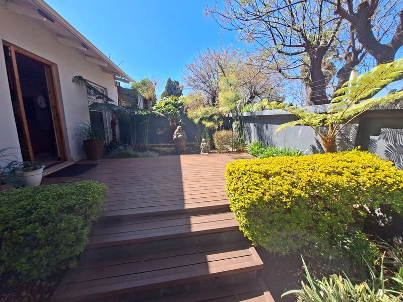 A well-maintained timber deck patio area featuring a landscaped garden, water feature, and secure boundary wall with electric fencing.