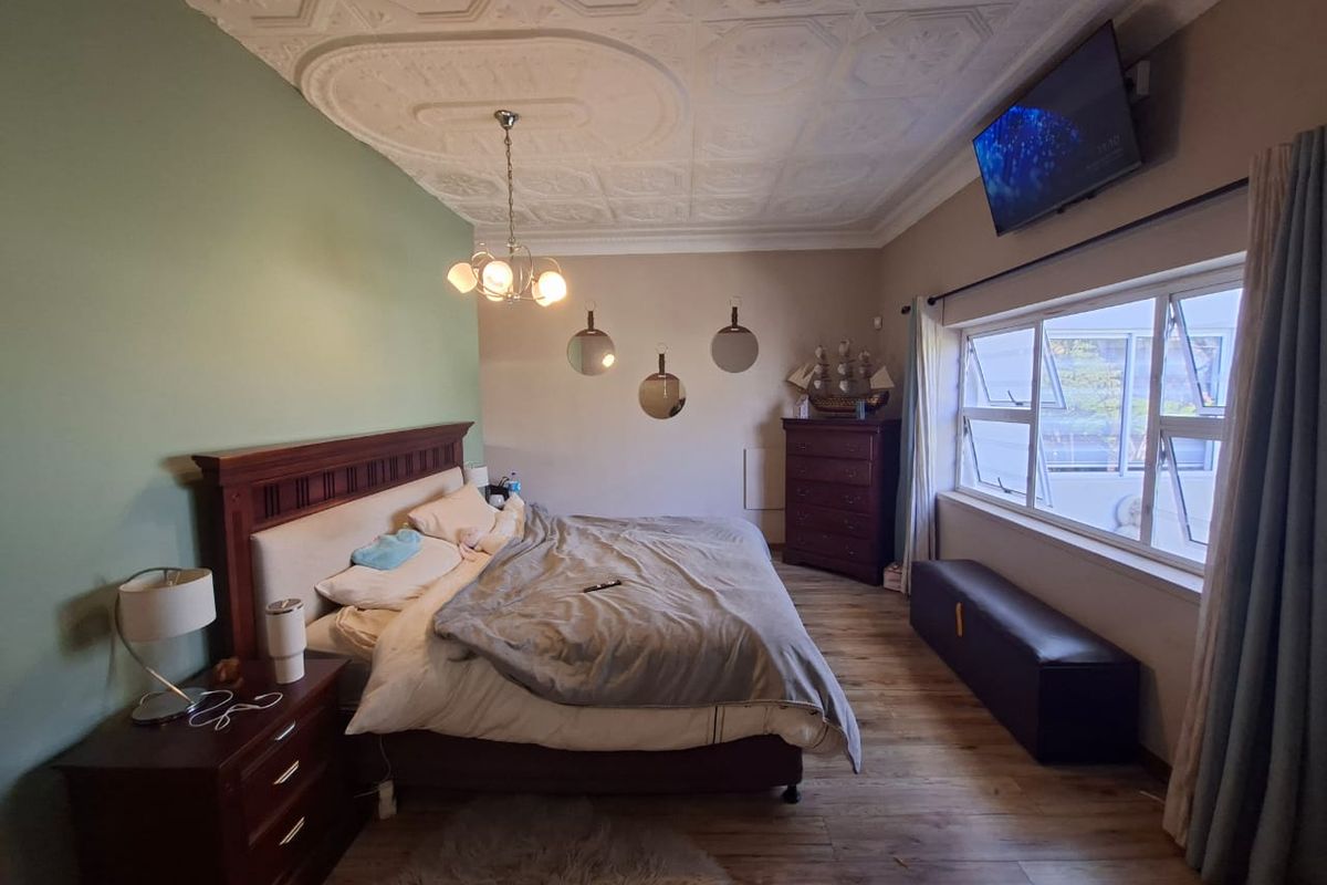 Spacious bedroom featuring a decorative pressed metal ceiling with a central ceiling rose, laminate flooring, and large casement windows providing natural light.