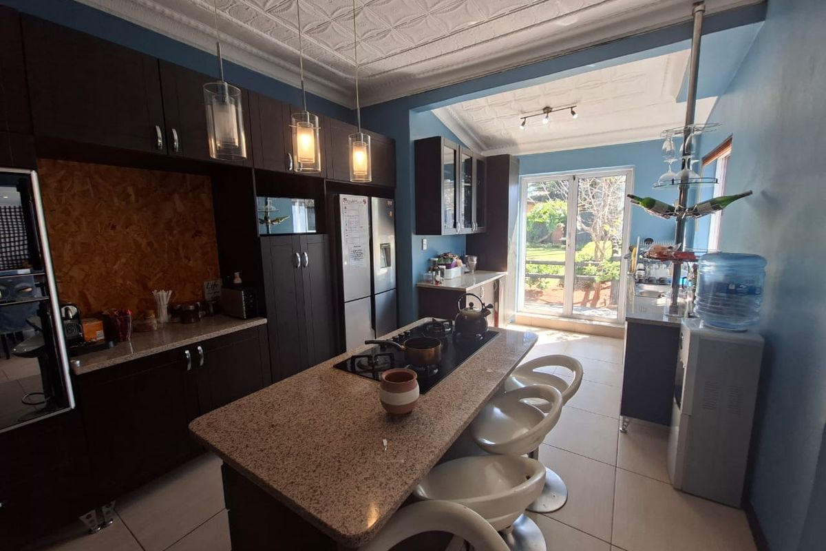 A well-appointed kitchen featuring dark cabinetry, granite countertops, a central island with a gas hob, and elegant pressed metal ceilings with pendant lighting.