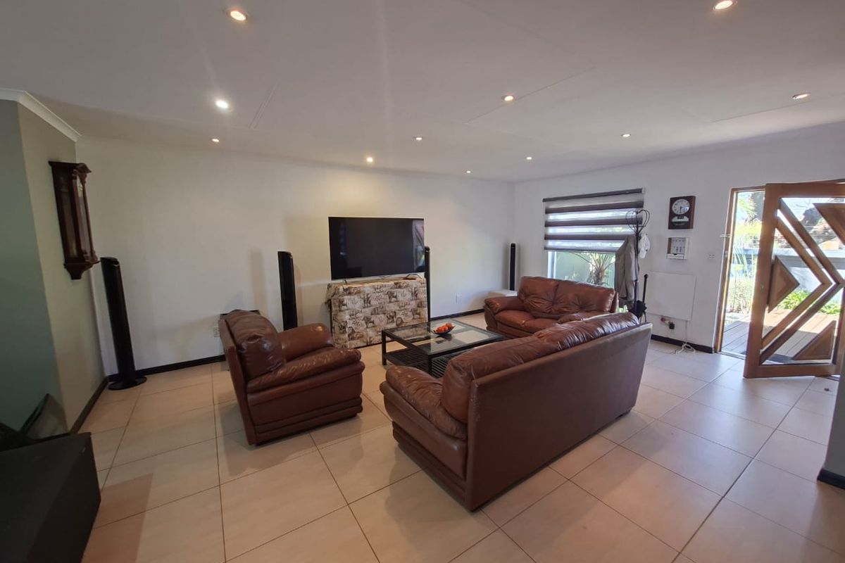 Spacious living room featuring neutral tiled flooring, recessed downlighting, and a timber entrance door with glass detailing.