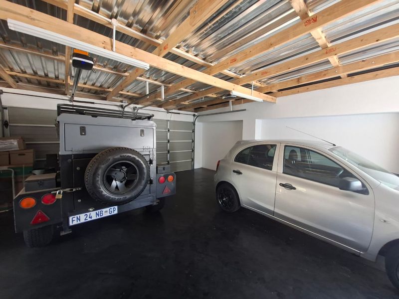 Spacious double garage featuring exposed timber roof trusses, corrugated metal ceiling, and a durable epoxy-coated concrete floor with an automated door system.