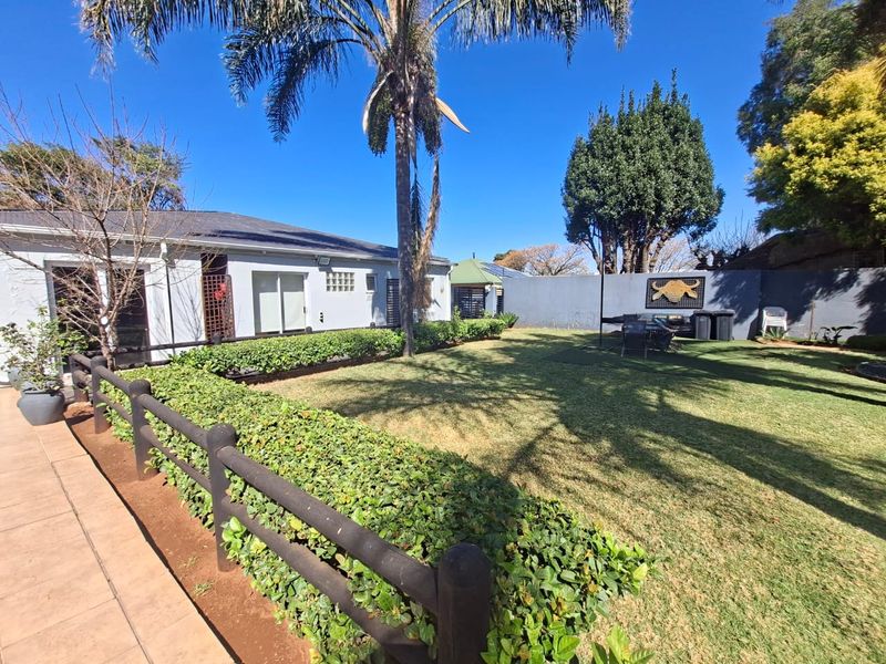 A well-maintained rear garden featuring a tiled patio area, manicured lawn, established palm tree, and secure boundary walling.