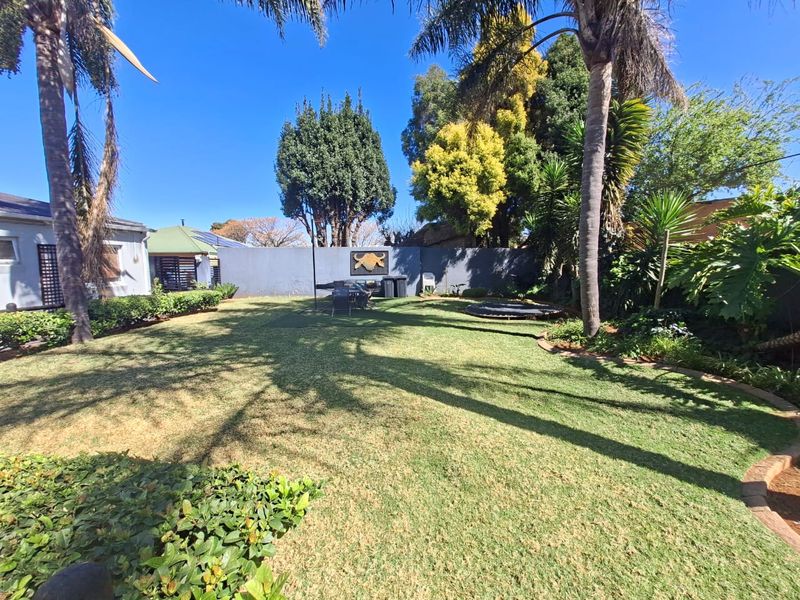 A well-maintained private garden featuring a lush lawn, mature palm trees, and a solid perimeter wall, providing a pleasant outdoor space.