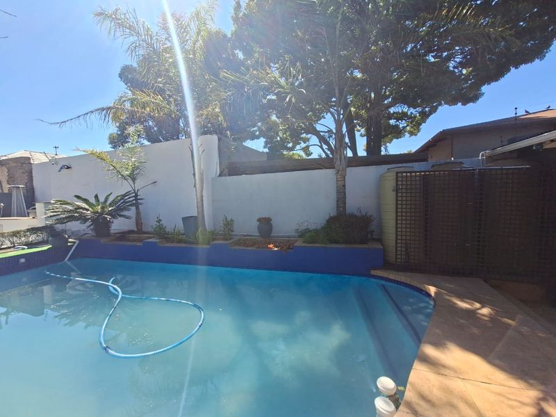 Outdoor pool area featuring a swimming pool with tiled surround, raised garden beds, and a boundary wall with an integrated water storage tank.