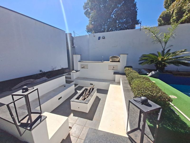 Outdoor entertainment area featuring a built-in fire pit, integrated seating, and a built-in braai, adjacent to a swimming pool.
