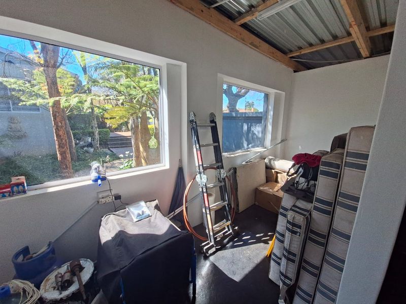 A utility space or storage area featuring concrete floors, exposed timber rafters, and large windows overlooking the garden, currently used for storage.