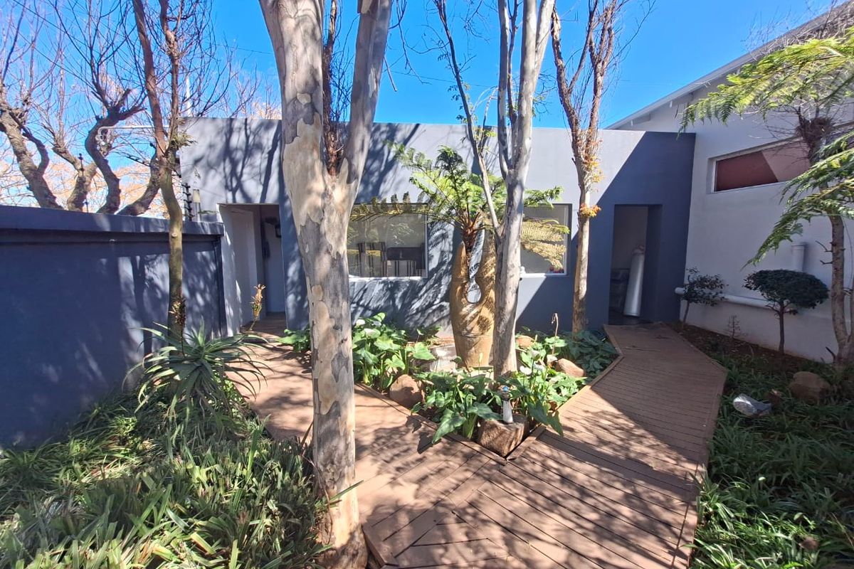 A well-maintained rear garden area featuring timber decking pathways, mature trees, and landscaped garden beds enclosed by a boundary wall.