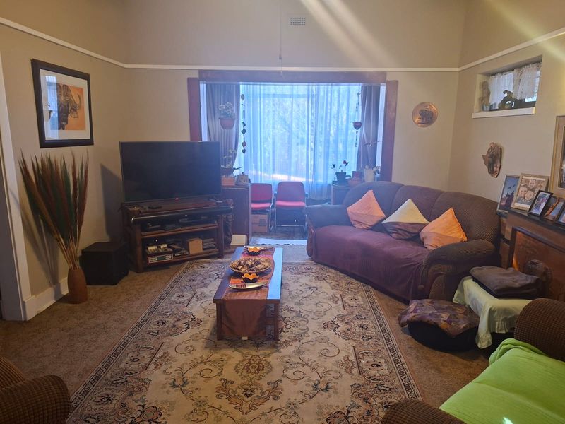 A comfortable living room featuring a large window, picture rails, and neutral wall tones, offering a functional space for relaxation.