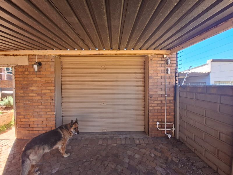 A functional garage space featuring a roller shutter door, brick walls, and a corrugated metal roof, providing secure covered parking.