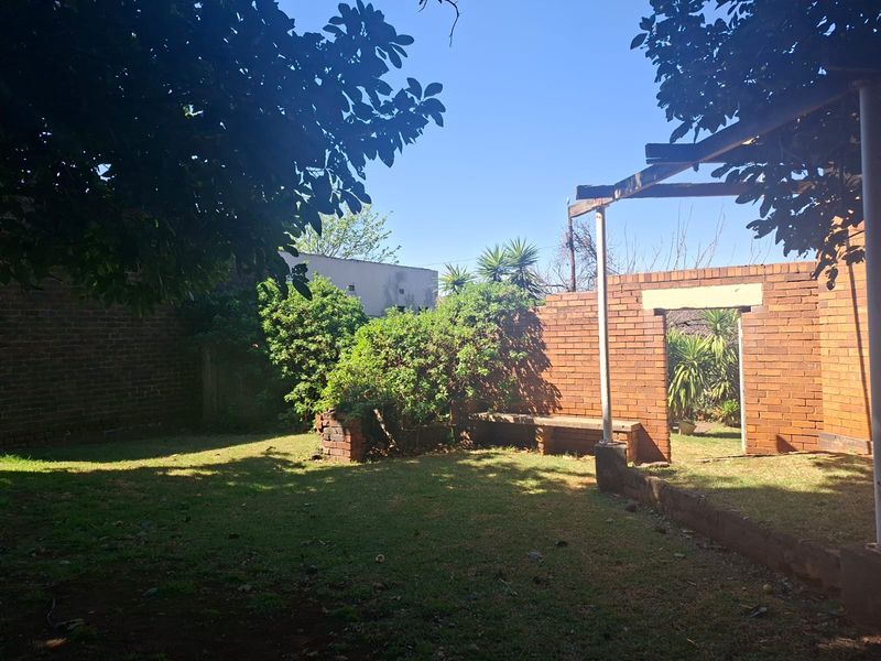 A private rear garden featuring a lawn, brick boundary walls, a built-in brick bench, and a partially constructed pergola structure.