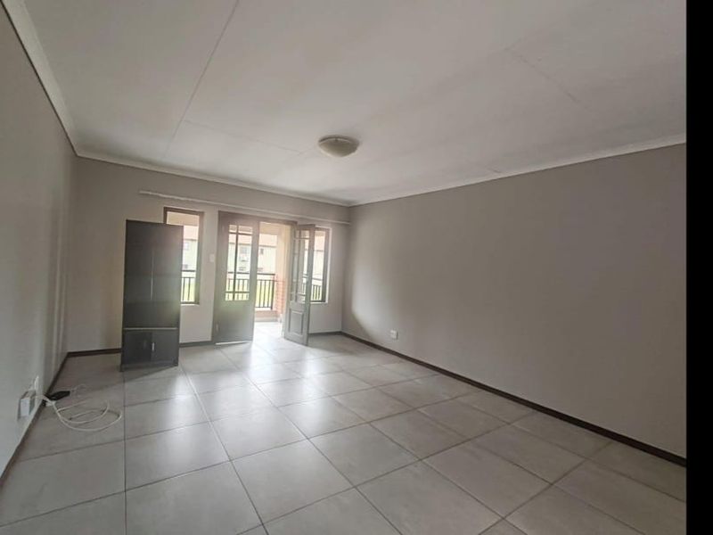 A spacious, empty living room featuring neutral tiled flooring and a glass-panelled door leading to an outdoor area.
