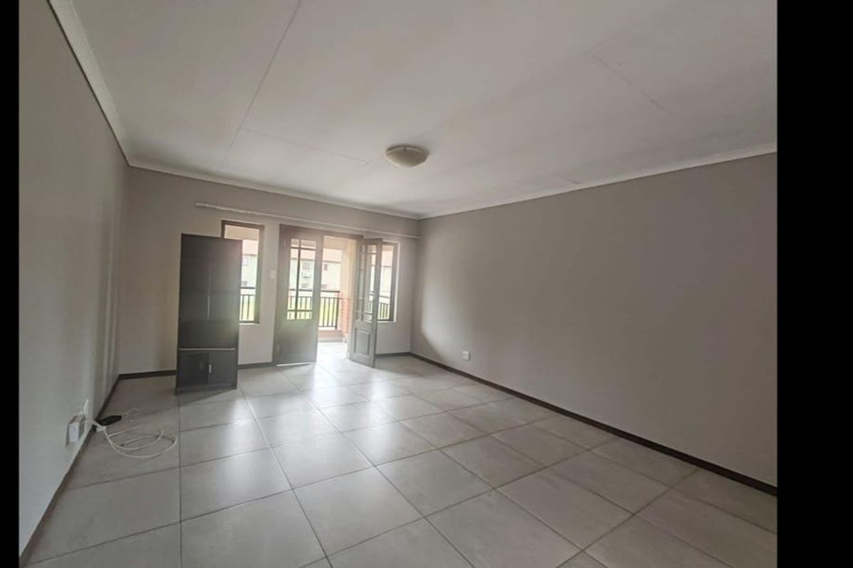 A spacious, empty living room featuring neutral tiled flooring and a glass-panelled door leading to an outdoor area.