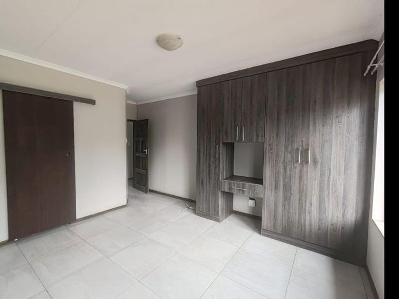 A clean, empty bedroom featuring modern dark wood-grain built-in cupboards, tiled flooring, and a sliding door entrance.