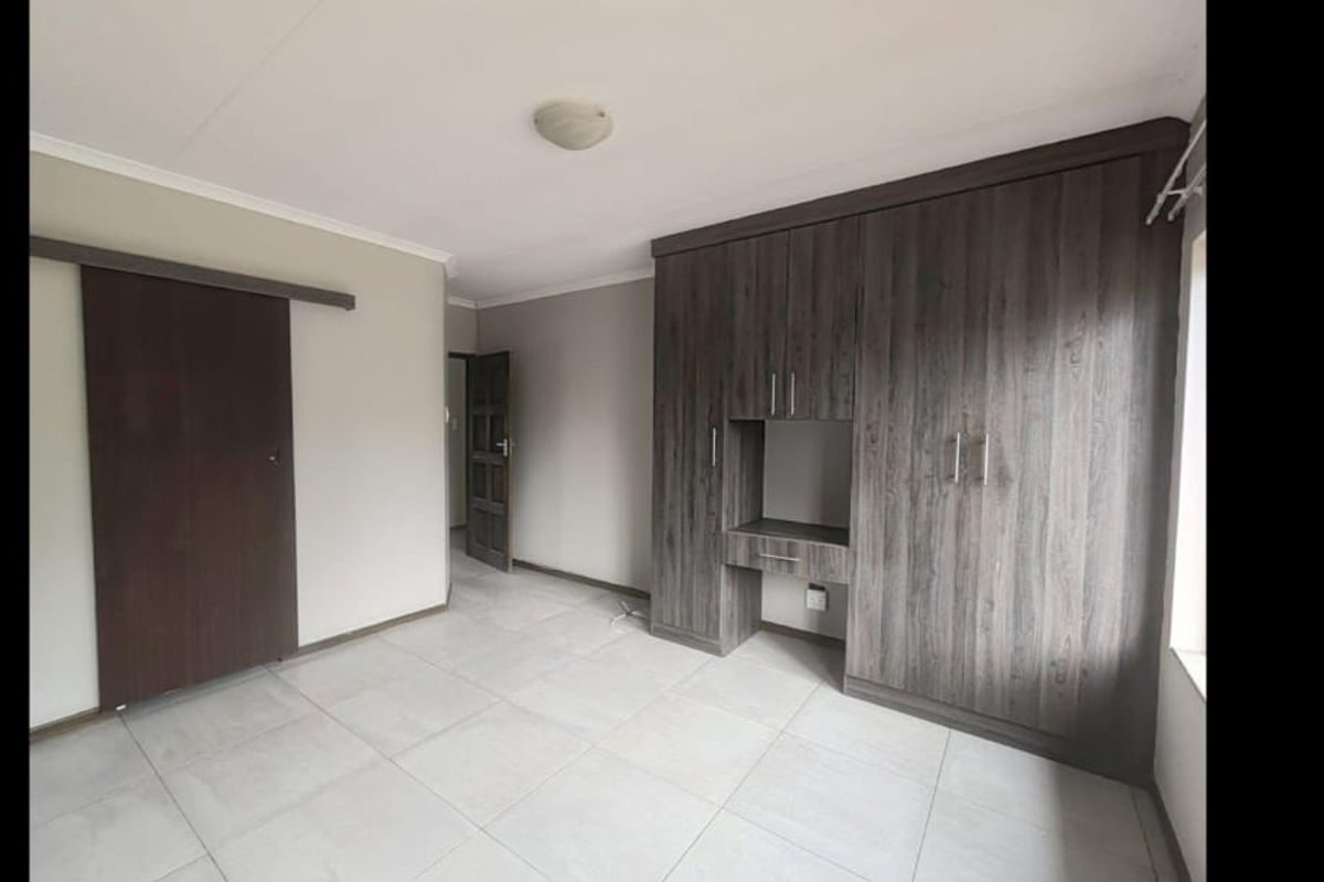 A clean, empty bedroom featuring modern dark wood-grain built-in cupboards, tiled flooring, and a sliding door entrance.