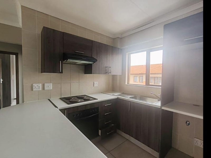 A functional kitchen featuring dark wood cabinetry, an electric hob with extractor, stainless steel sink, and a breakfast counter with tiled finishes.