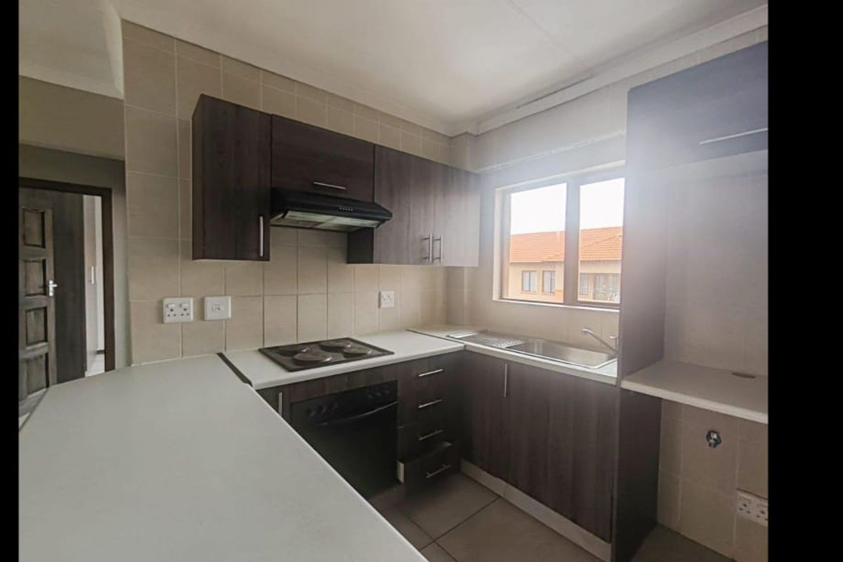 A functional kitchen featuring dark wood cabinetry, an electric hob with extractor, stainless steel sink, and a breakfast counter with tiled finishes.