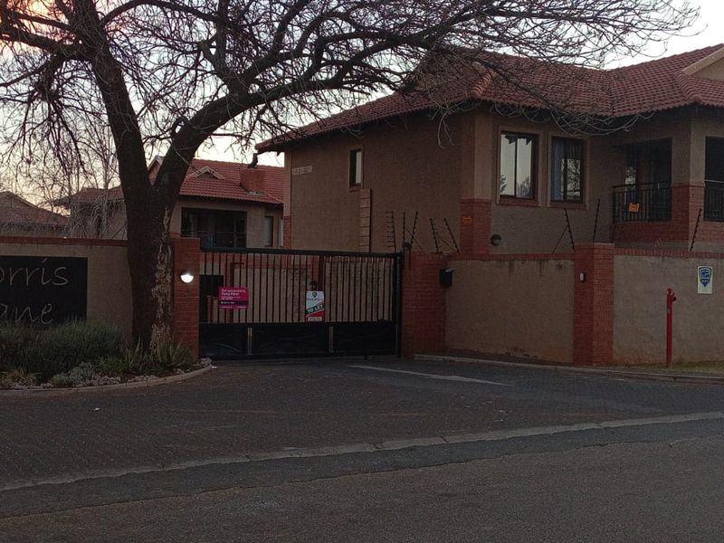 Exterior view of the Morris Lane apartment complex entrance, featuring a secure gated access point, brick boundary walls, and electric fencing.