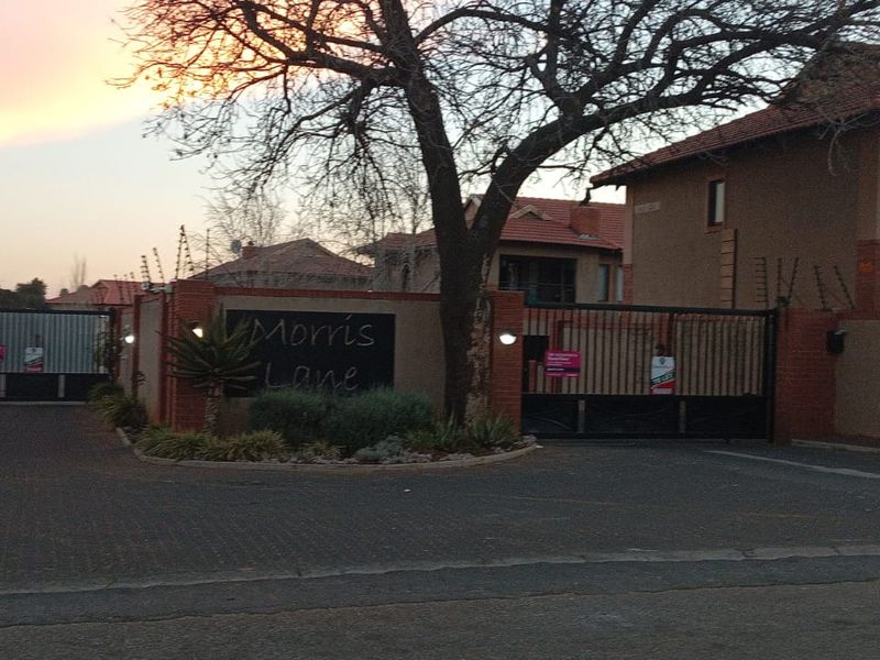 Front entrance view of Morris Lane apartment complex featuring secure gated access, brick boundary walls, and electric fencing.