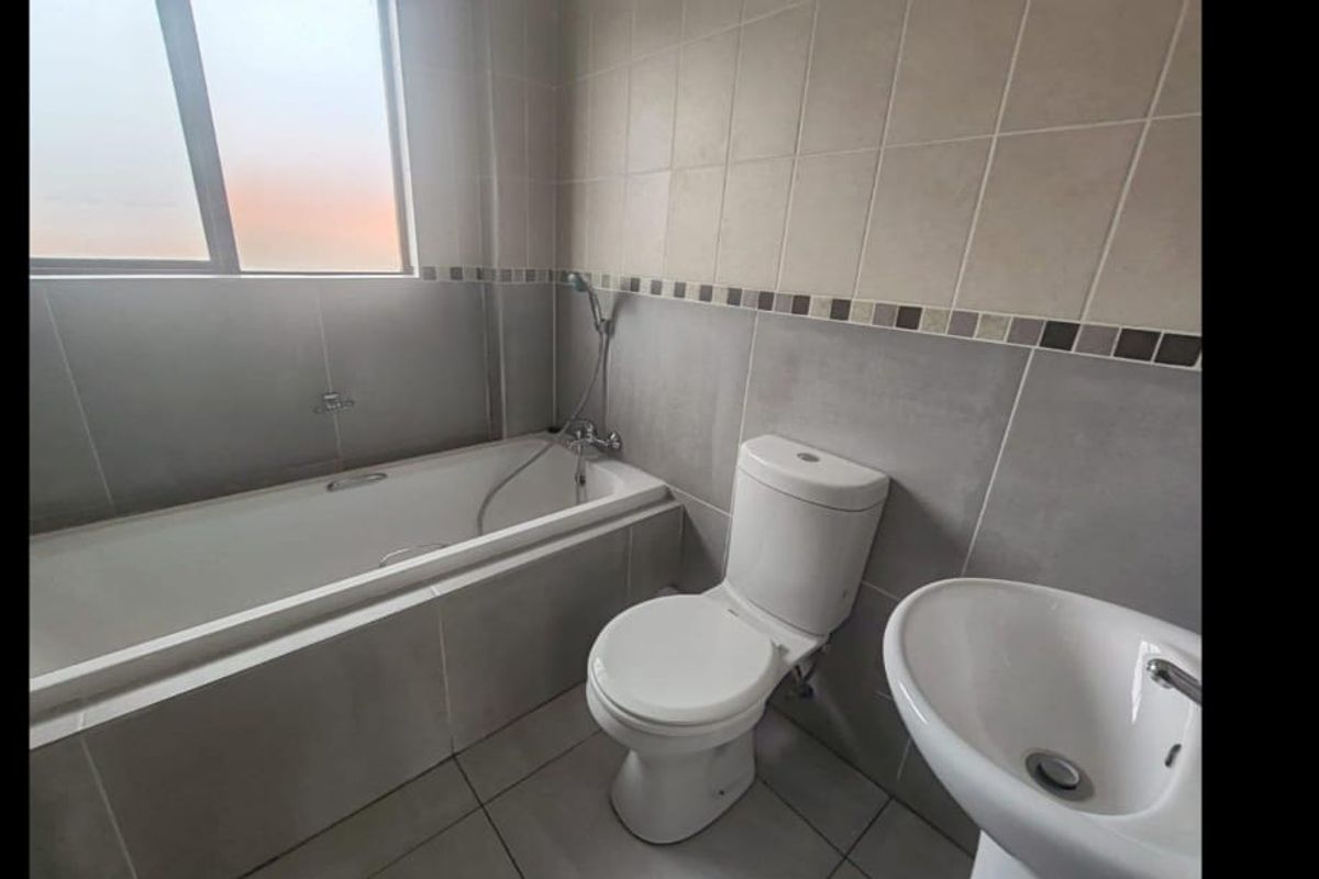A functional bathroom featuring a bathtub, pedestal basin, and toilet with neutral wall and floor tiling.