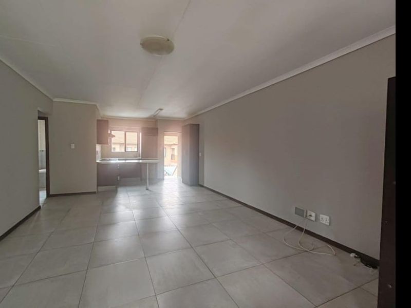 An open-plan living and kitchen area featuring neutral tiled flooring and built-in cabinetry, offering a blank canvas for interior design.