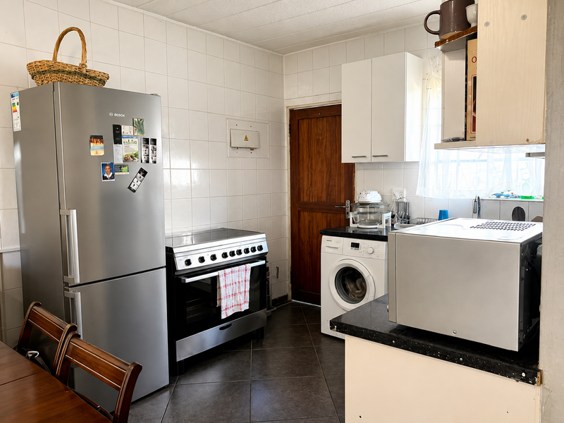 A functional kitchen featuring tiled walls, dark tiled flooring, black granite countertops, and built-in cabinetry with space for a washing machine and oven.