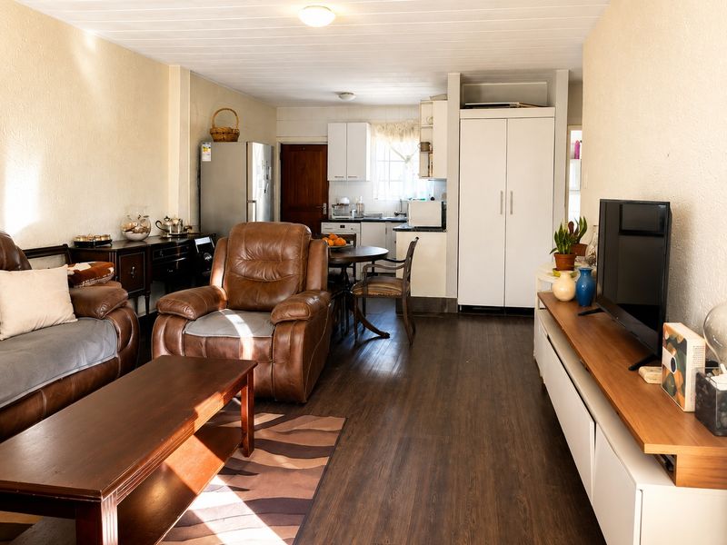 Open-plan living area featuring dark laminate flooring, a compact kitchen with white cabinetry, and a built-in storage cupboard.